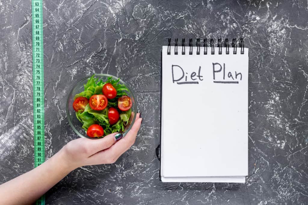 notebook-for-diet-plan-salad-and-measuring-tape-on-grey-stone-table-top-view