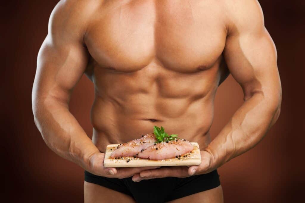 Muscular man holding plate with meat, food for bodybuilder 