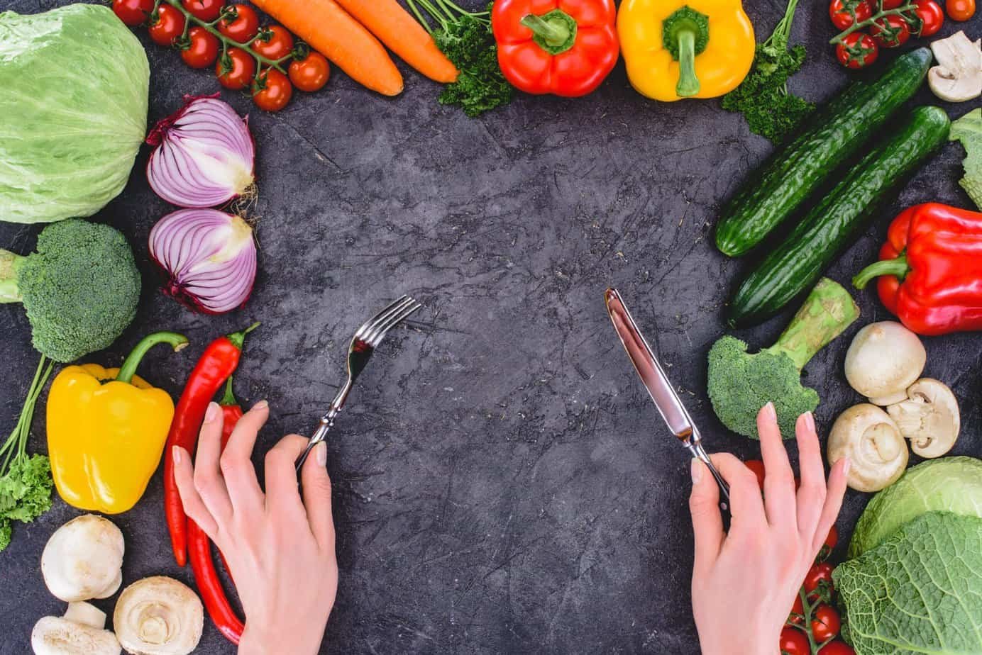 Cropped shot of hands holding fork and knife above healthy fresh vegetables on black